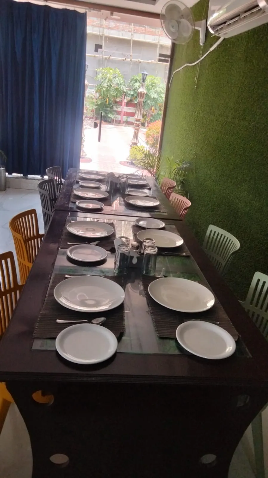 Restaurant patio tables set for dining, with grey and yellow chairs against the turf wall
